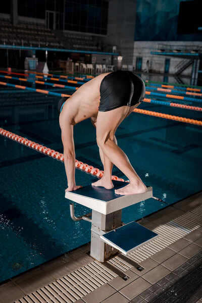swimmer standing in starting pose near swimming pool 