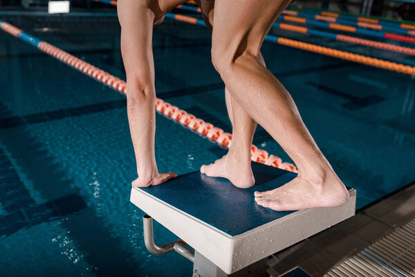 cropped view of man standing in starting pose near swimming pool 