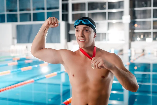 happy champion in swimming cap gesturing while holding golden medal