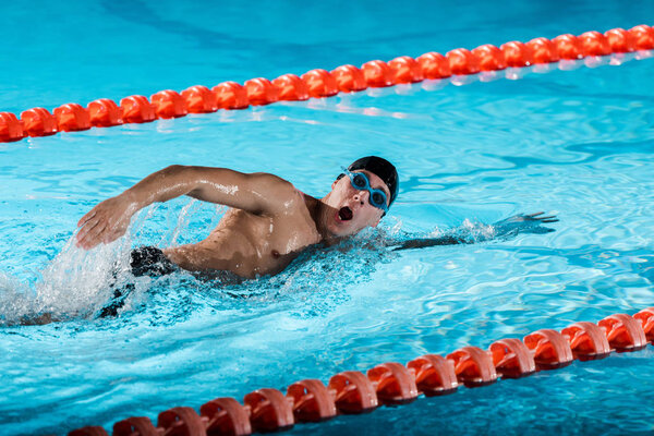 drops of water near swimmer with opened mouth training in swimming pool 