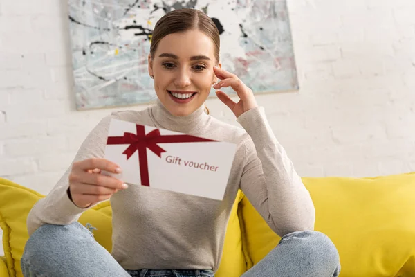 Attraente Donna Sorridente Possesso Buono Regalo Sul Divano — Foto Stock