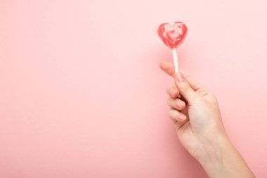 Kırpılmış pembe arka planda kalp şeklinde lolipop tutan kadın görüntüsü 
