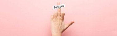 panoramic shot of woman showing middle finger and card with sexism lettering on pink background  clipart