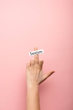 cropped view of woman showing middle finger and card with sexism lettering on pink background  clipart