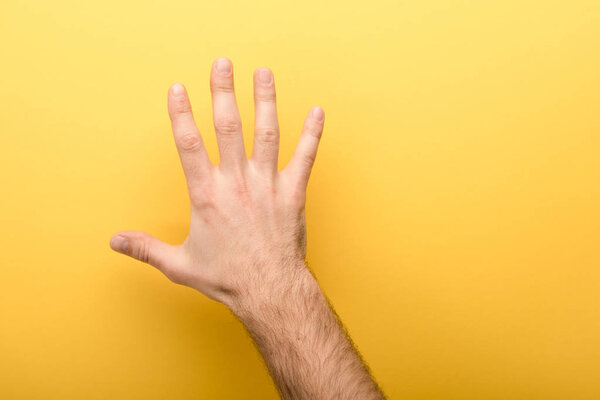 cropped view of man showing five fingers on yellow background 