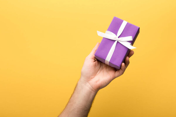 cropped view of man holding gift on yellow background 