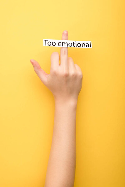 cropped view of woman showing middle finger and card with too emotional lettering on yellow background 