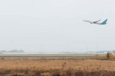 Bulutlu bir havada çimenli havaalanından kalkan uçak.