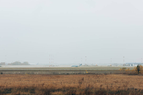 Grassy airfield with airplane on runway and cloudy sky