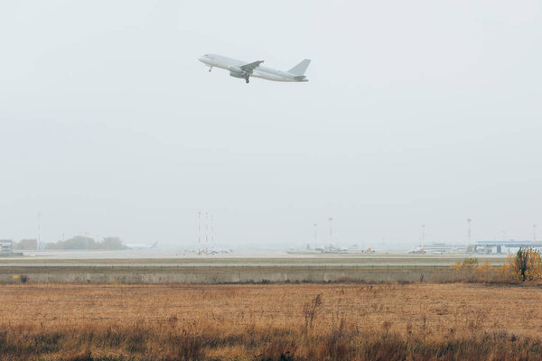 Airplane taking off above foggy airfield with runway