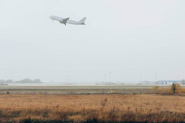 Самолет в облачном небе над аэродромом аэропорта с взлетно-посадочной полосой
