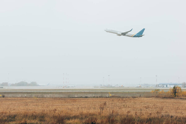 Вылет самолета в облачном небе над аэродромом с взлетно-посадочной полосой
