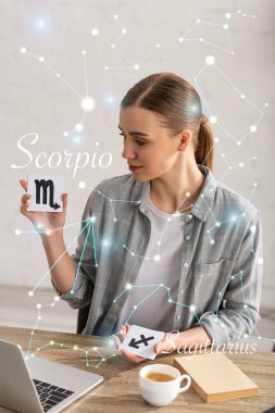 Astrologer holding cards with zodiac signs beside book, laptop and constellations  clipart