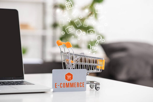 Toy cart beside credit card with e-commerce lettering and laptop on table