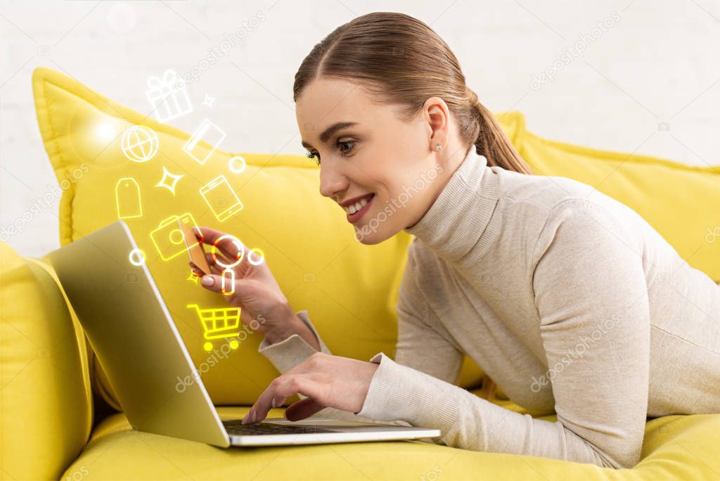 Side view of smiling woman using laptop and holding credit card beside illustration
