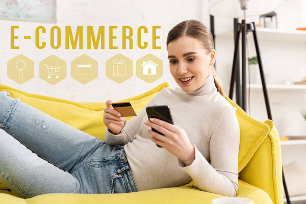 Улыбающаяся девушка с помощью смартфона и держащая кредитную карту на диване в гостиной, концепция e-commerce
