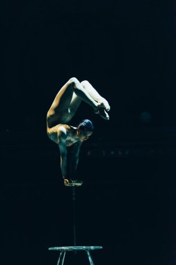 KYIV, UKRAINE - NOVEMBER 1, 2019: Female acrobat performing exercise in circus isolated on black clipart