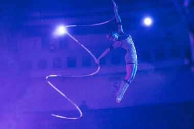 KYIV, UKRAINE - NOVEMBER 1, 2019: Air gymnast performing exercise in light of floodlights in circus  clipart