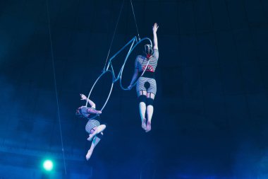 KYIV, UKRAINE - NOVEMBER 1, 2019: Low angle view of air gymnasts performing with metal rings in circus clipart