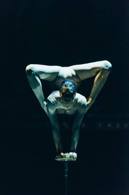 KYIV, UKRAINE - NOVEMBER 1, 2019: Flexible gymnast performing handstand in circus isolated on black clipart