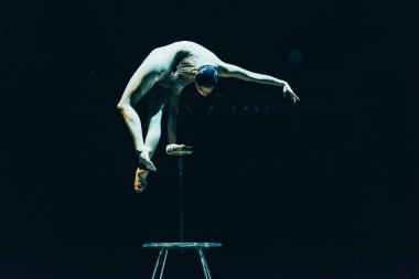 KYIV, UKRAINE - NOVEMBER 1, 2019: Female acrobat balancing on hand in circus isolated on black clipart