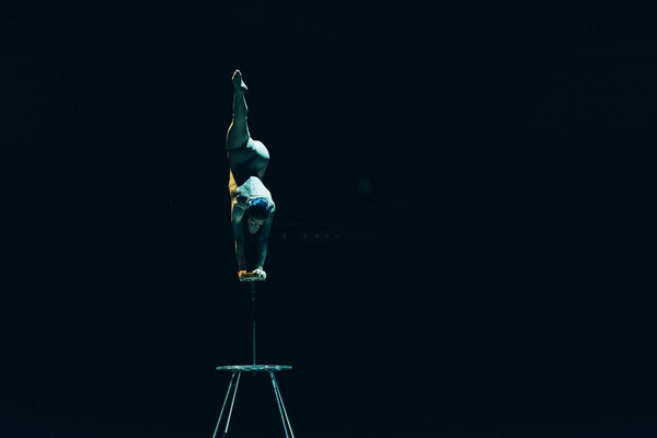 KYIV, UKRAINE - NOVEMBER 1, 2019: Back view of flexible acrobat balancing on hands in circus isolated on black