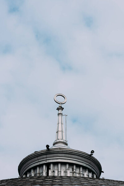 Low angle view of spire with circle on building with cloudy sky at background