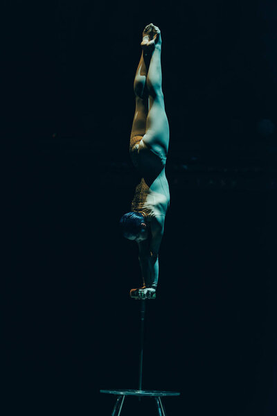 KYIV, UKRAINE - NOVEMBER 1, 2019: Gymnast performing handstand in circus isolated on black