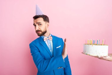 cropped view of woman holding birthday cake near businessman showing no gesture on pink 