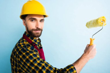 Mavi kasklı mutlu tamirci elinde boya silindiri tutuyor. 