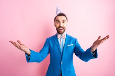 Heyecanlı, parti şapkalı, elleri açık pembe kameraya bakan iş adamı. 