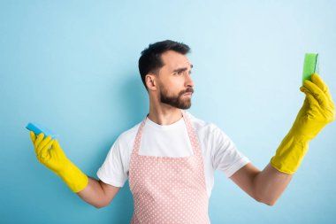 Lastik eldivenli ciddi bir adam mavi üzerine sünger bakıyor. 