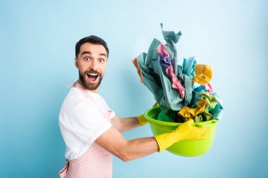 Kirli çamaşırları mavi olan plastik bir leğen tutan heyecanlı bir adam. 