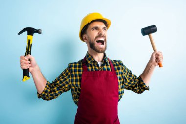 Mavi kasklı kızgın işçi elinde çekiçlerle 