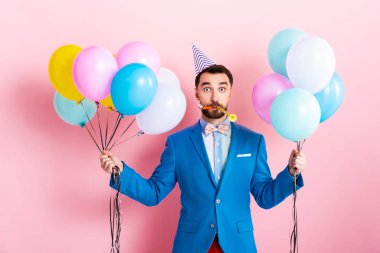 Parti şapkalı iş adamı elinde pembe balonlar tutuyor. 