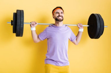 sportsman working out with heavy barbell on yellow