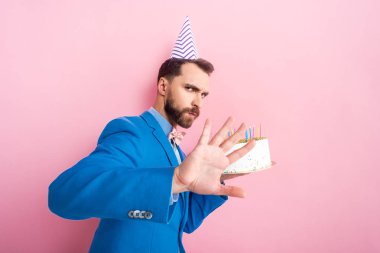 bearded man showing no gesture while holding birthday cake isolated on pink 