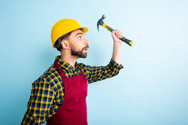 side view of surprised workman holding hummer isolated on blue 