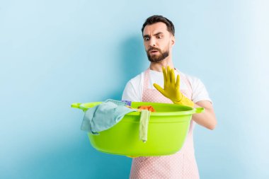 Elinde kirli çamaşırlarla plastik kase tutan ve mavi üzerine dur işareti yapan şok olmuş bir adam. 
