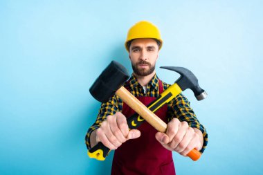 selective focus of workman holding hammers on blue  clipart