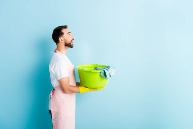 Kirli çamaşırları mavi üzerinde tutan mutlu sakallı adamın yan görünüşü 