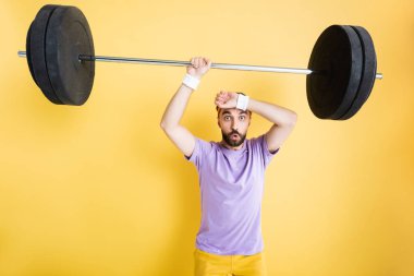 Yorgun sporcu sarı halterle ağır halter tutuyor.