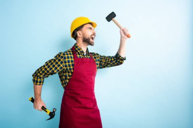 Mavi üzerine çekiç tutan kızgın işçinin yan görünüşü 