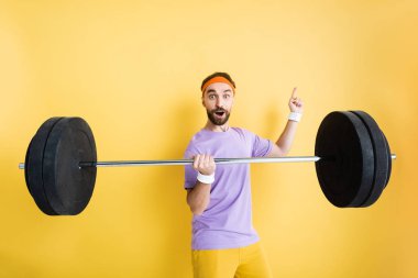surprised sportsman pointing with finger and holding barbell on yellow clipart