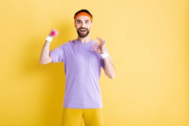 Neşeli sporcu küçük bir dambıl tutuyor ve sarı üzerinde 