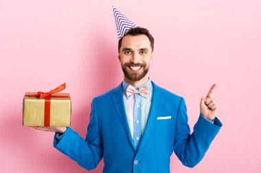 Takım elbiseli mutlu işadamı hediyesini tutuyor ve parmağıyla pembeyi işaret ediyor. 