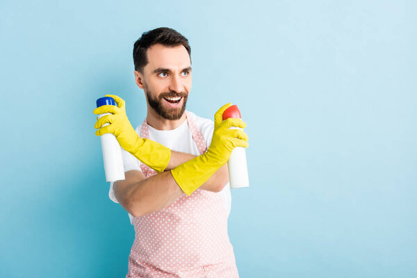 cheerful bearded man holding spray bottles on blue 