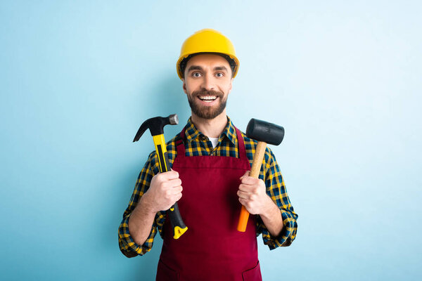 cheerful bearded workman holding hammers on blue 
