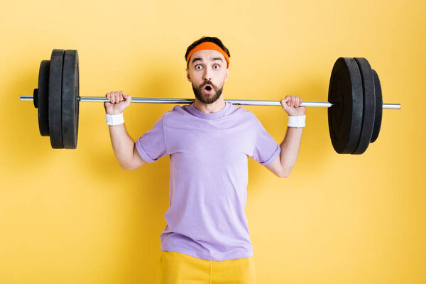 shocked sportsman working out with barbell on yellow