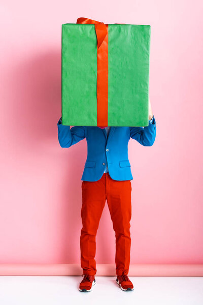 man in suit covering face while holding huge present on pink 